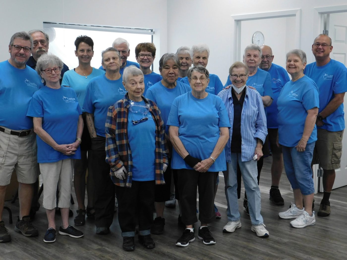 A large group of Leesburg Food Bank volunteers in matching blue Leesburg Food Bank t-shirts, gathered indoors.